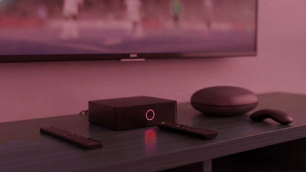 A streaming stick, a set-top box and a round streaming box with their remotes on a TV console