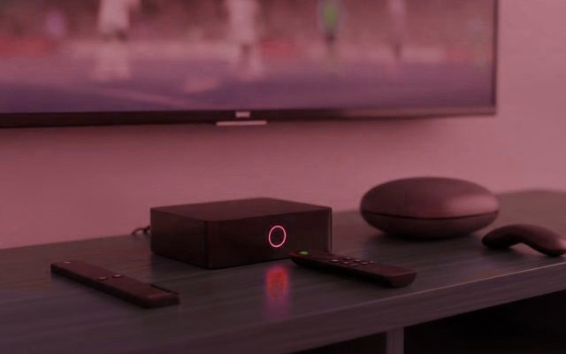 A streaming stick, a set-top box and a round streaming box with their remotes on a TV console