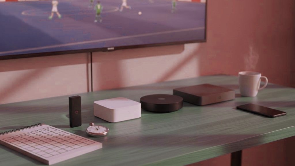 Five streaming devices, a notebook scoring grid and a stopwatch in front of a TV showing a football match
