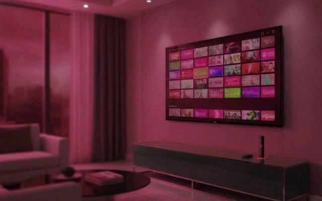 A living-room TV showing an IPTV channel guide with a streaming stick on the console